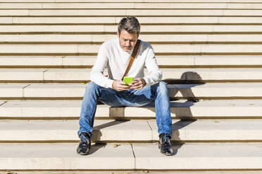 Lässiger Geschäftsmann, der auf einer Treppe sitzt und Nachrichten auf seinem Smartphone liest - GIOF05621