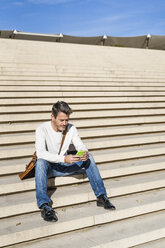 Lässiger Geschäftsmann, der auf einer Treppe sitzt und Nachrichten auf seinem Smartphone liest - GIOF05623