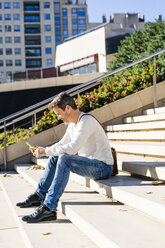 Lässiger Geschäftsmann, der auf einer Treppe sitzt und Nachrichten auf seinem Smartphone liest - GIOF05624