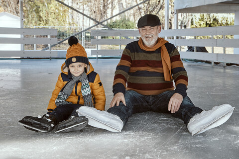Großvater und Enkel auf der Eislaufbahn, auf dem Eis sitzend, lizenzfreies Stockfoto