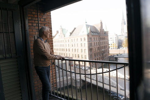 Germany, Hamburg, Speicherstadt, senior businessman standing at the window with view over the city - JOSF02887