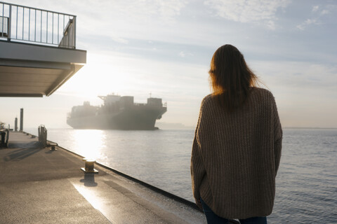 Germany, Hamburg, woman standing on pier at the Elbe shore with container ship in background stock photo