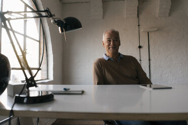 Porträt eines lächelnden älteren Geschäftsmannes, der am Schreibtisch im Büro sitzt - JOSF02889