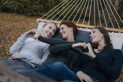 Happy mother with two teenage girls lying in hammock in garden in autumn stock photo
