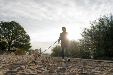 Germany, Hamburg, woman walking with dog on beach at the Elbe shore - JOSF02896