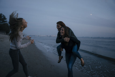 Germany, Hamburg, carefree mother with two teenage girls on the beach at Elbe shore at night - JOSF02901