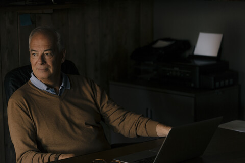 Älterer Geschäftsmann mit Laptop sitzt am Schreibtisch im Büro, lizenzfreies Stockfoto