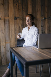 Geschäftsfrau am Schreibtisch sitzend mit einem Glas Wasser und einem Laptop - JOSF02910
