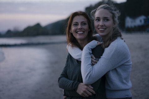 Deutschland, Hamburg, glückliche Mutter und Teenager-Mädchen umarmen sich am Abend am Elbufer, lizenzfreies Stockfoto