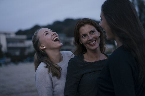 Deutschland, Hamburg, glückliche Mutter mit zwei Teenager-Mädchen am Strand am Elbufer am Abend - JOSF02921