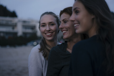 Deutschland, Hamburg, glückliche Mutter mit zwei Teenager-Mädchen am Strand am Elbufer am Abend, lizenzfreies Stockfoto