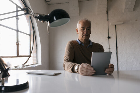 Älterer Geschäftsmann mit Tablet am Schreibtisch im Büro, lizenzfreies Stockfoto