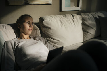 Ernstes Teenager-Mädchen mit Tablet auf der Couch sitzend zu Hause - JOSF02939