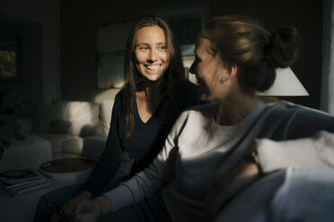 Two happy teenage girls with cell phone sitting on couch at home - JOSF02942