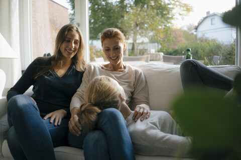Happy mother with two teenage girls on couch at home stock photo