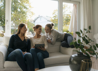 Glückliche Mutter mit zwei Mädchen im Teenageralter, die zu Hause auf der Couch ein Tablet benutzen - JOSF02946