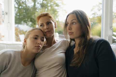 Mother with two teenage girls relaxing on couch at home stock photo