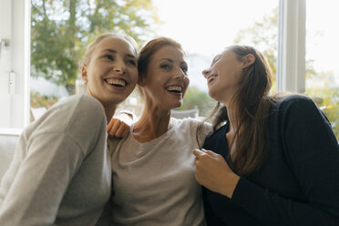 Happy mother with two teenage girls on couch at home - JOSF02948