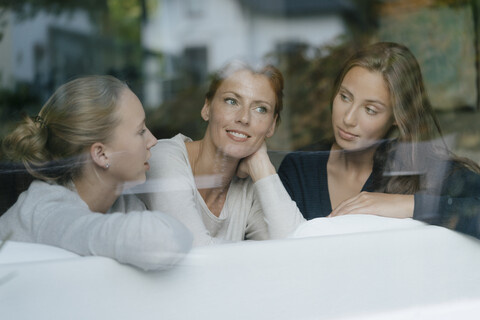 Mother with two teenage girls on couch at home behind windowpane stock photo