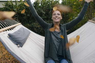 Carefree woman in hammock throwing autumn leaves - JOSF02959