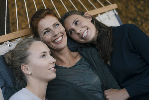 Happy mother with two teenage girls lying in hammock in garden in autumn - JOSF02962