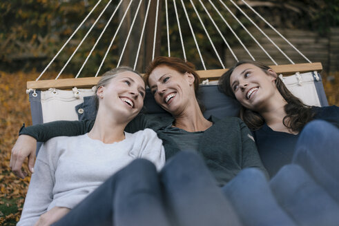 Happy mother with two teenage girls lying in hammock in garden in autumn - JOSF02964