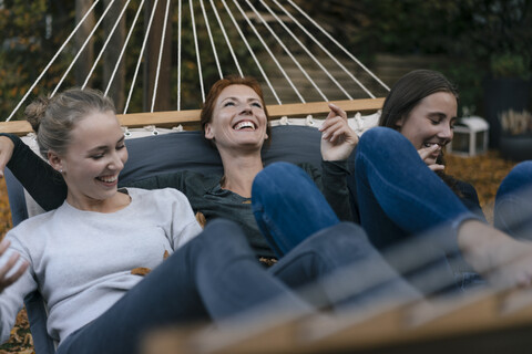 Unbekümmerte Mutter mit zwei Mädchen im Teenageralter in der Hängematte im Garten liegend im Herbst, lizenzfreies Stockfoto