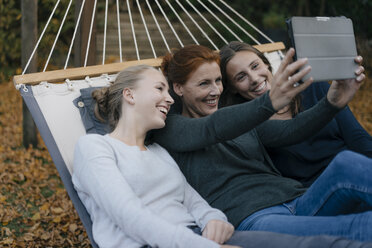 Glückliche Mutter mit zwei Mädchen im Teenageralter liegt in der Hängematte im Garten im Herbst mit Tablet - JOSF02968