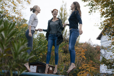 Happy mother with two teenage girls jumping on trampoline in garden in autumn - JOSF02970