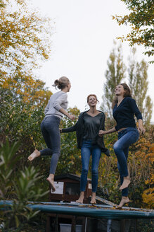 Glückliche Mutter mit zwei Mädchen im Teenageralter, die im Herbst im Garten auf dem Trampolin springen - JOSF02971