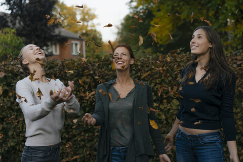 Unbekümmerte Mutter mit zwei Mädchen im Teenageralter, die Herbstblätter im Garten werfen, lizenzfreies Stockfoto