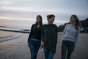 Germany, Hamburg, happy mother with two teenage girls walking on the beach at Elbe shore in the evening - JOSF02976