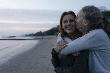 Germany, Hamburg, mother and teenage girl hugging on the beach at Elbe shore in the evening - JOSF02978