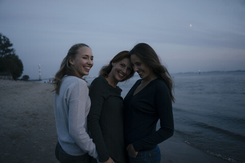 Germany, Hamburg, happy mother with two teenage girls on the beach at Elbe shore in the evening stock photo