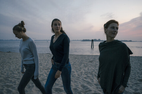 Germany, Hamburg, mother with two teenage girls walking on the beach at Elbe shore in the evening stock photo