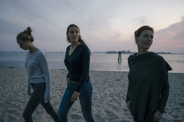 Germany, Hamburg, mother with two teenage girls walking on the beach at Elbe shore in the evening - JOSF02981