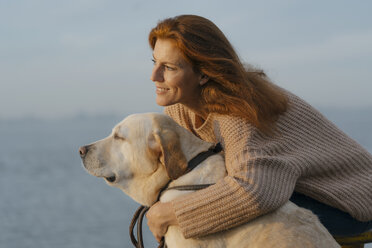Germany, Hamburg, happy woman cuddling with dog at the Elbe shore - JOSF02983
