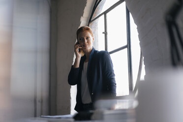 Businesswoman on cell phone at the window in office - JOSF02995