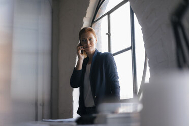 Geschäftsfrau am Handy am Fenster im Büro - JOSF02995