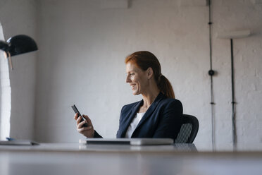 Glückliche Geschäftsfrau mit Mobiltelefon am Schreibtisch im Büro - JOSF03001