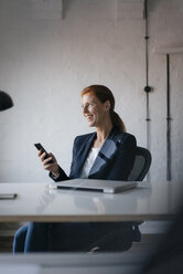 Happy businesswoman with cell phone at desk in office - JOSF03002