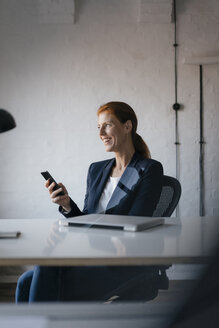 Glückliche Geschäftsfrau mit Mobiltelefon am Schreibtisch im Büro - JOSF03002