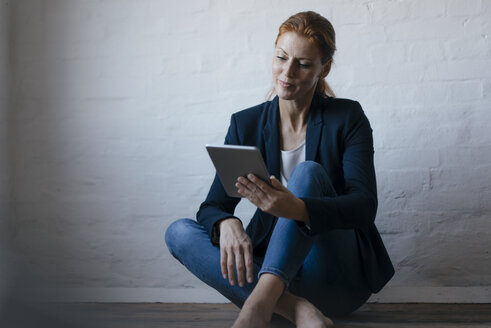 Barfüßige Geschäftsfrau, die im Büro auf dem Boden sitzt und ein Tablet benutzt - JOSF03012