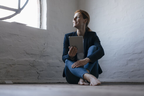 Barfüßige Geschäftsfrau, die im Büro auf dem Boden sitzt und ein Tablet benutzt - JOSF03014