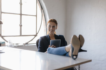 Businesswoman using tablet with feet on desk in office - JOSF03016