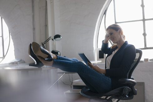 Businesswoman using tablet with feet on desk in office - JOSF03017