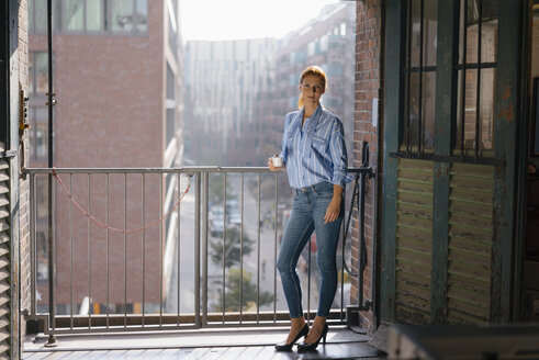 Germany, Hamburg, Speicherstadt, businesswoman with cup of coffee standing at the window with view over the city - JOSF03023