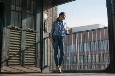 Germany, Hamburg, Speicherstadt, businesswoman with cup of coffee standing at the window with view over the city - JOSF03024