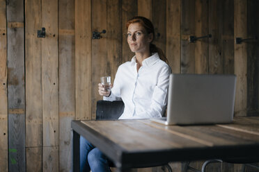 Geschäftsfrau am Schreibtisch sitzend mit einem Glas Wasser und einem Laptop - JOSF03029