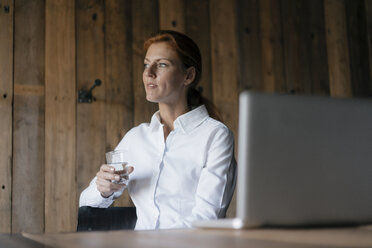 Geschäftsfrau am Schreibtisch sitzend mit einem Glas Wasser und einem Laptop - JOSF03030